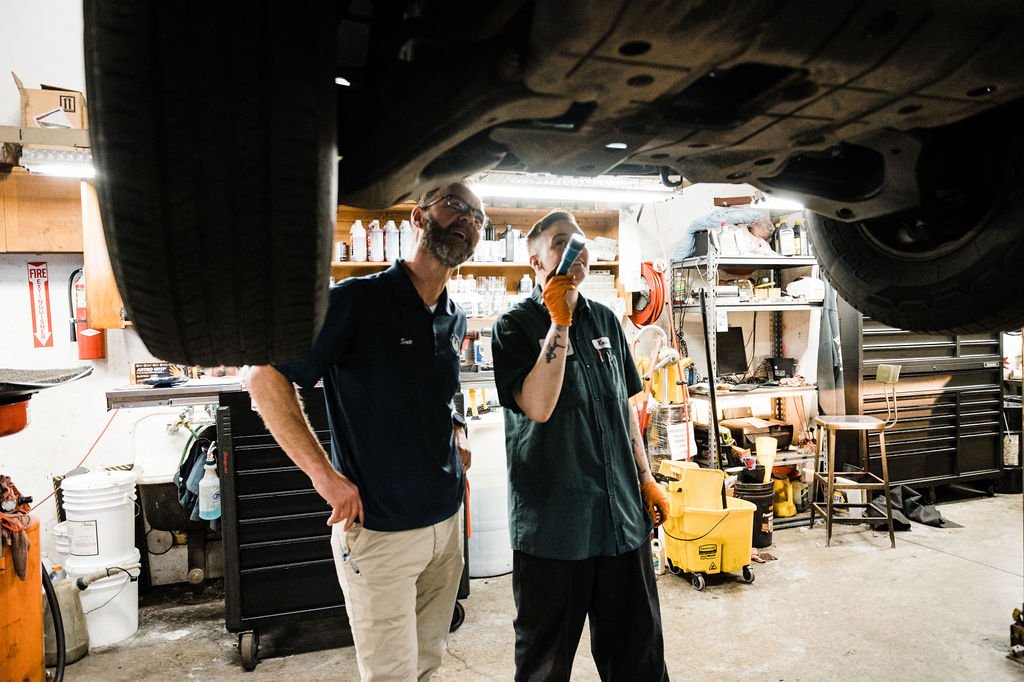 Two professionals inspecting the underside of a car in a garage captured in commercial brand photography.
