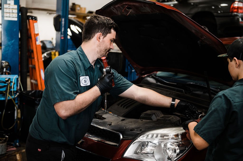 Two technicians inspecting and fixing a car in a garage, using Auto tools and protective gears.