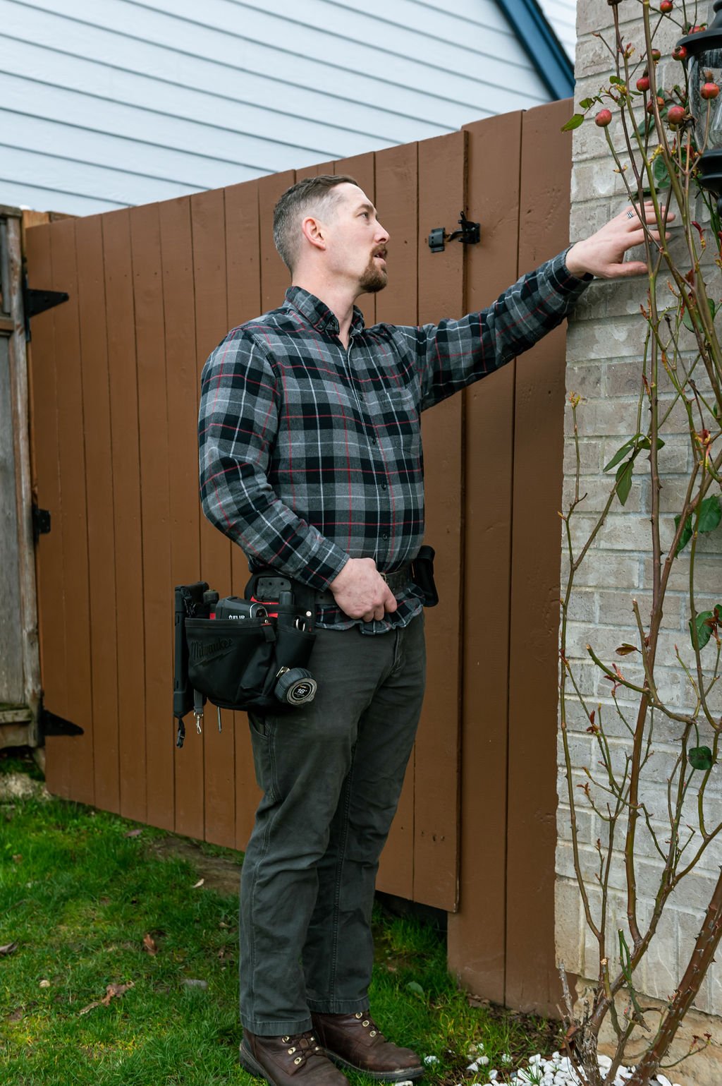 A man in a plaid shirt and jeans standing next to a fence posing for the CDO Inspections branding photoshoot.