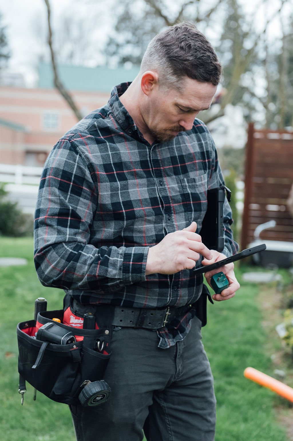 An expert man conducting a property inspection, standing in front of a house with a tablet and devices.