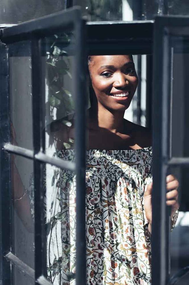 A woman wearing a Roma Label brand dress happily peering through a window.