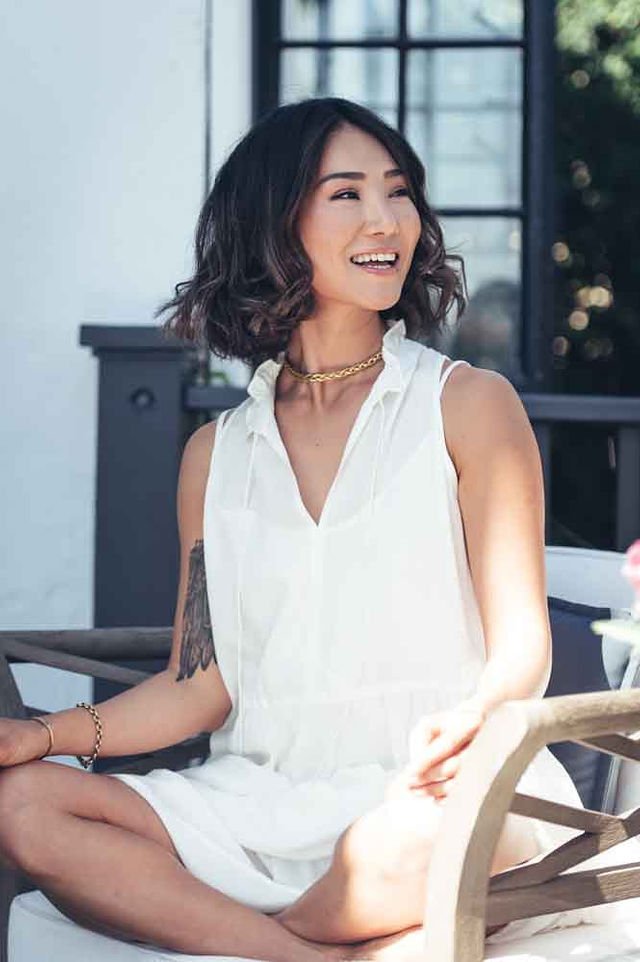  In a business branding photoshoot, a woman sits on a chair, crossing her legs and wearing a bright smile, projecting professionalism and warmth
