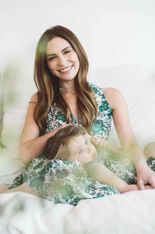 A mother in a green dress sits on a bed with a child beside her.