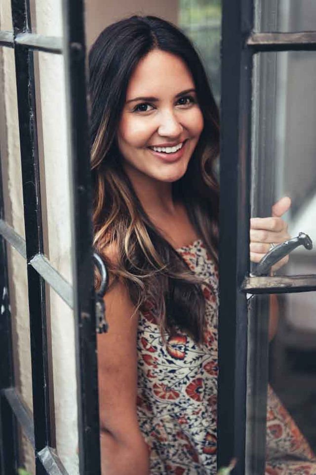 A woman with a warm smile looking through a window. Photographed by a clothing brand photographer.