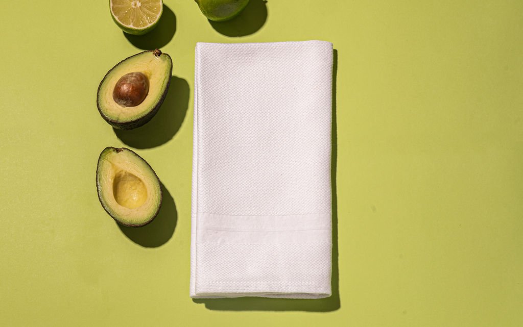 A brand photographer in Portland captured an image of an avocado, lime, and a cotton napkin on a green background.