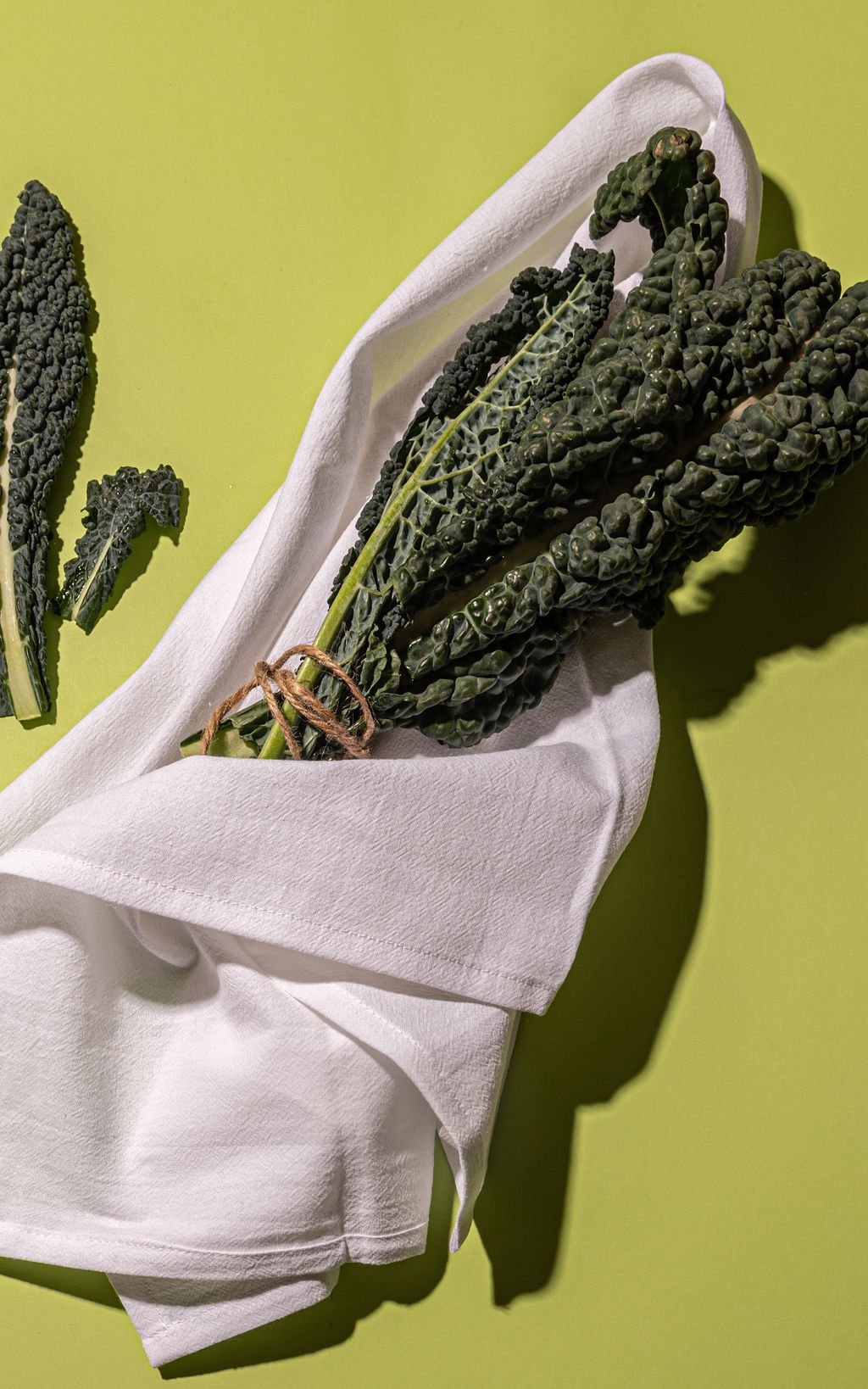 A bunch of kale wrapped in a white kitchen towel, branded ALT LINEN, placed on a kitchen countertop.