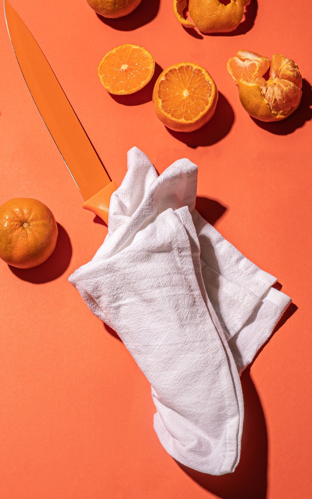 Brand photography featuring a knife, oranges, and a luxurious linen napkin on a red surface.
