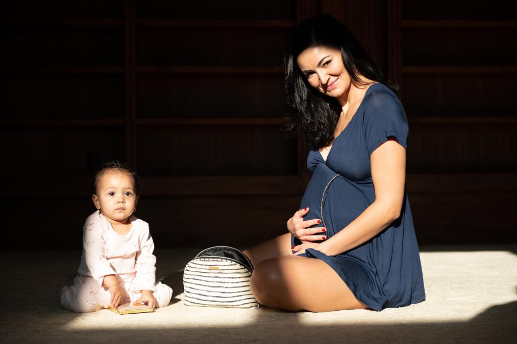 A pregnant woman and her baby sit on the floor posing for Pregjama in a Portland brand photoshoot