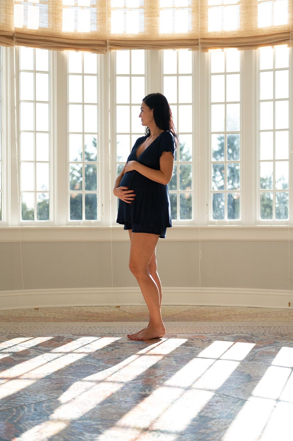A pregnant woman admiring the view through a large window wearing Pregjama brand maternity loungewear.