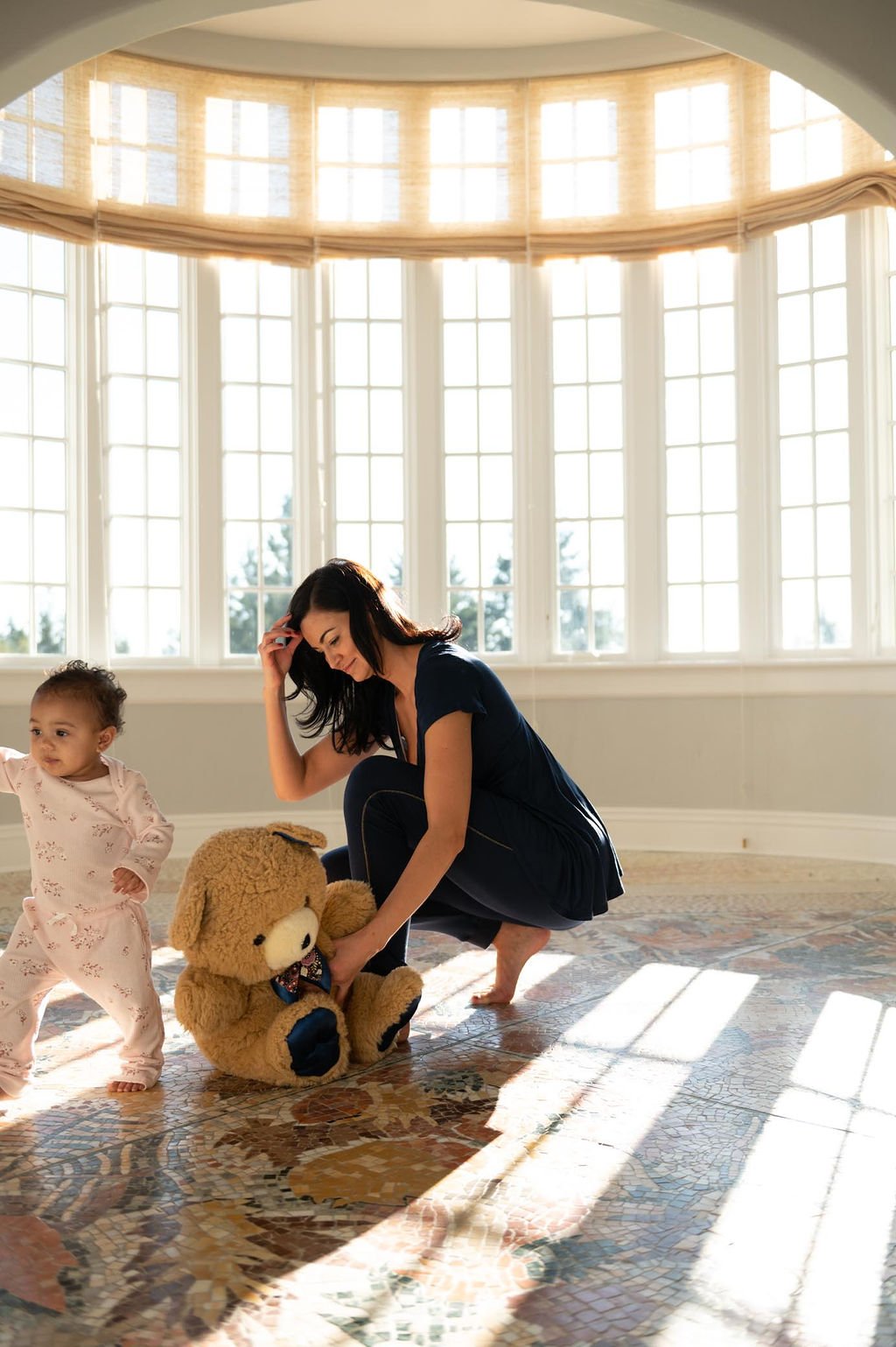 A mother and her child are happily playing with a teddy bear in a cozy room.