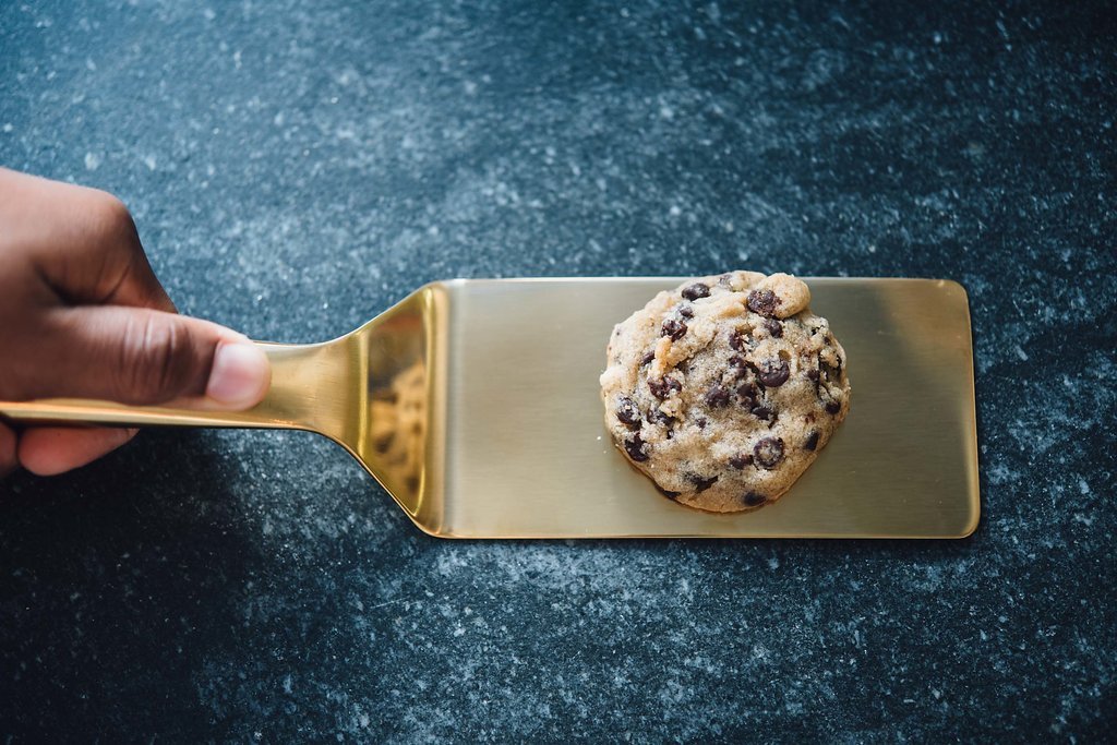 A chef holding a golden colored spatula over a cookie, adds a touch of elegance to the art of baking.