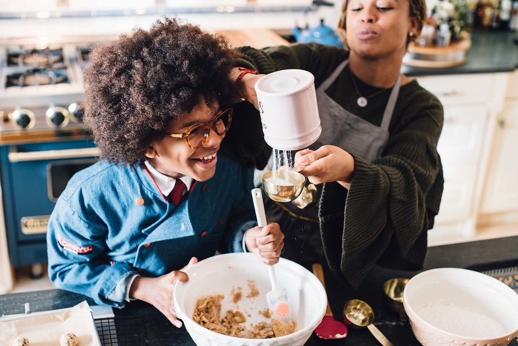 A chef with her child, captured by a Portland branding photographer, mixing ingredients for cookies in a bowl.