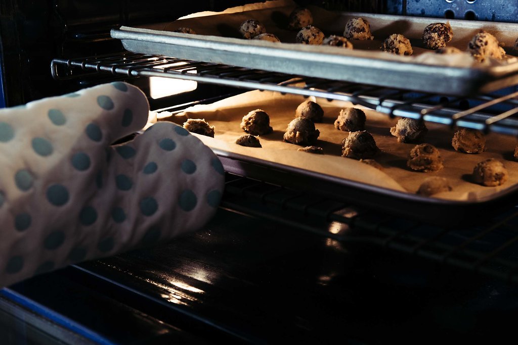 A person wearing a polka dot oven mitt carefully removes freshly baked cookies from the oven.