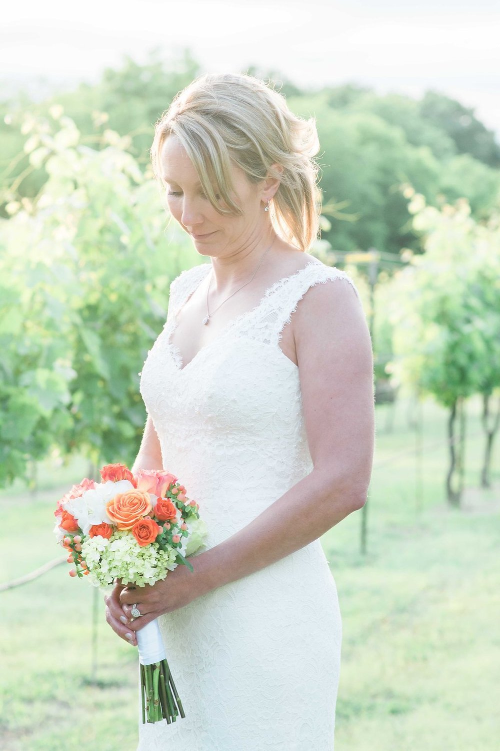A beautiful bride in a white wedding dress posing for an event photograph in a vineyard.jpg
