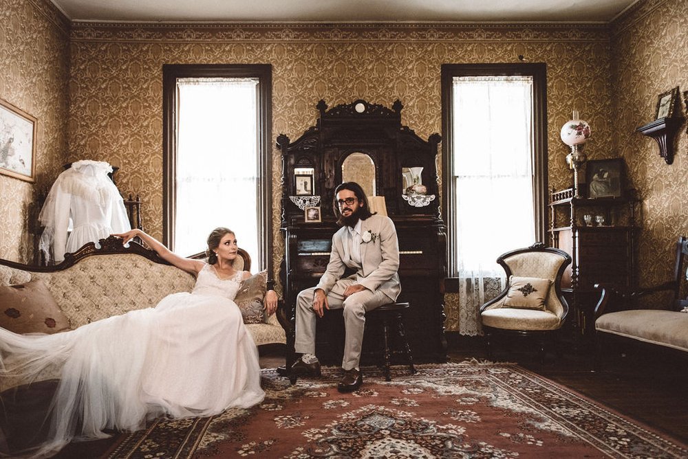 A bride and groom elegantly pose in a vintage room, captured by an event photographer.jpg