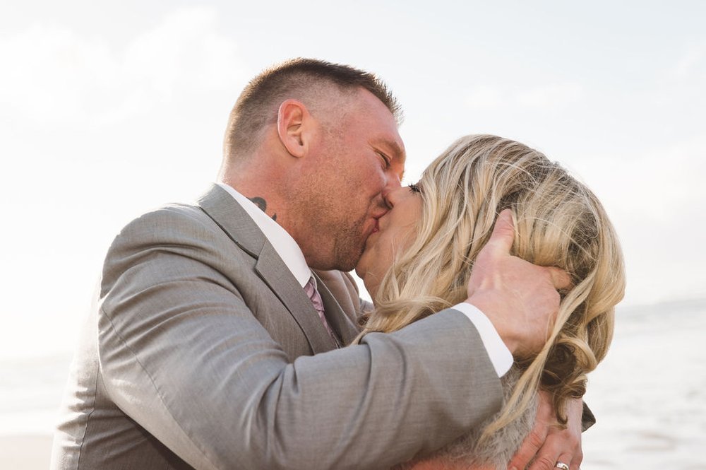 A bride and groom share a romantic kiss on the beach, captured by a wedding event.jpg