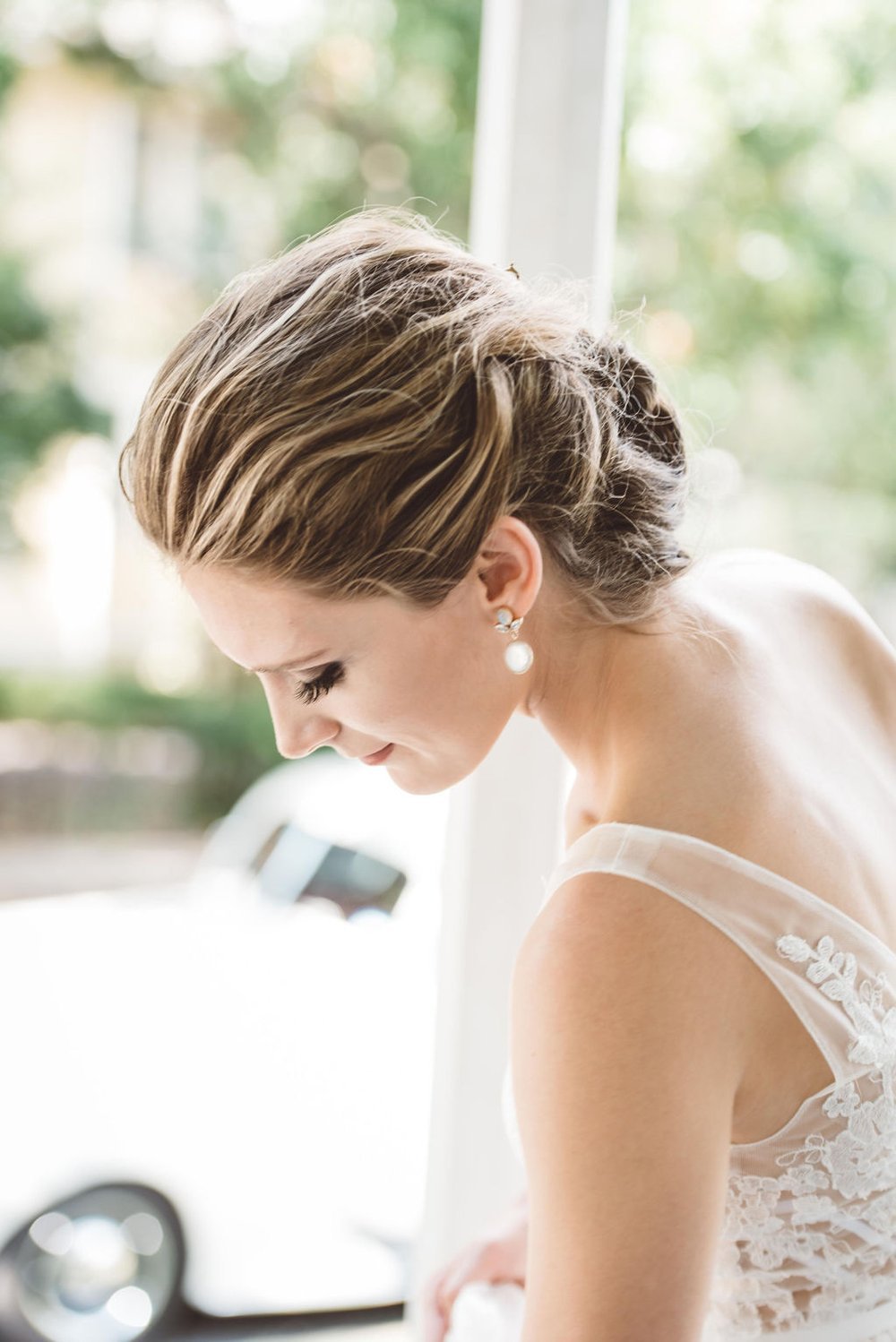 A bride in a lace dress gazes out the window, filled with anticipation and excitement for her.jpg