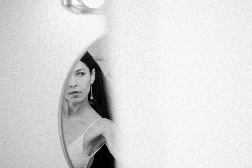 A woman in a white dress admiring her reflection in a mirror, captivated by her own beauty.jpg