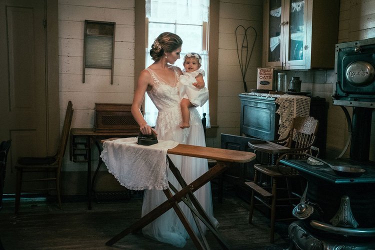 A bride cradles a baby in a vintage kitchen. A photograph by an event photographer.jpg
