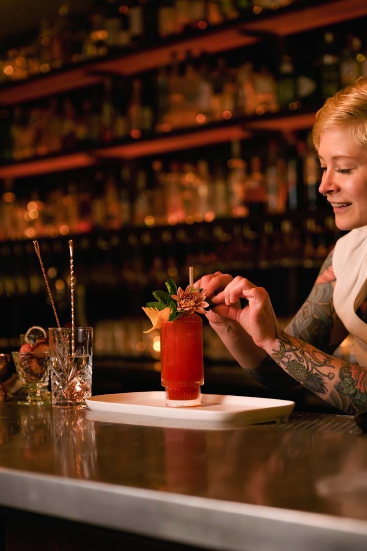 An image of a woman with tattoos sitting at a bar, savoring a drink, beautifully captured in a photograph.jpg