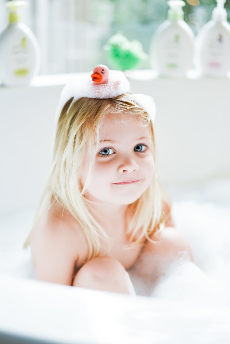 A joyful little girl posing for a product photographer in Portland and enjoying a bubble-filled bath in a bathtub.jpg