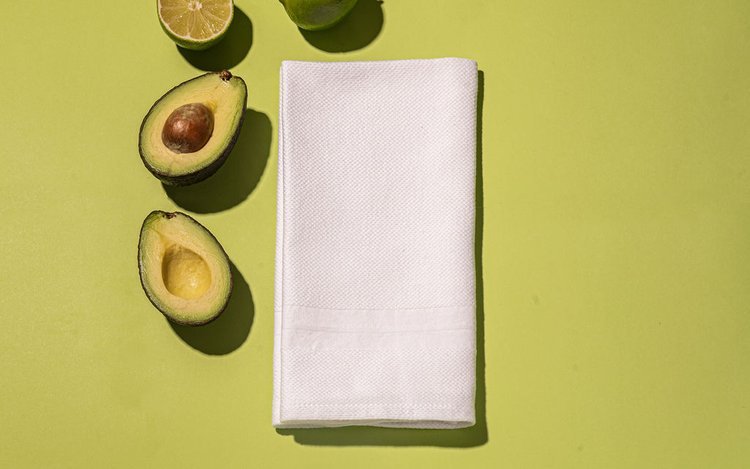 A white napkin with a fresh avocado and lime resting on a vibrant green surface in product photography session.jpg