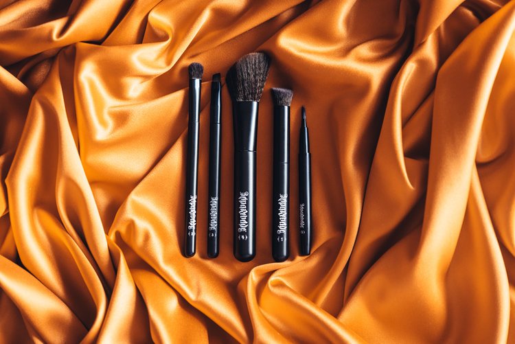 Three makeup brushes on orange satin cloth, showcasing cosmetic product photography.jpg