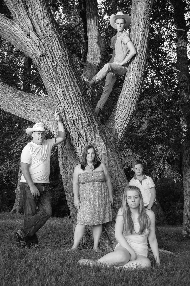 A family of four smiling and posing for a portrait before a tree. Captured by a professional family photographer in Portland.jpg