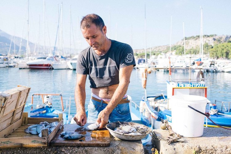 A man is preparing fish on a table in front of a marina. Captured by a travel photographer from Portland during her visit to various places.jpg