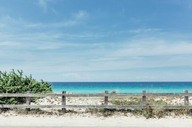 A serene beach with a wooden fence and crystal-clear blue water..jpg