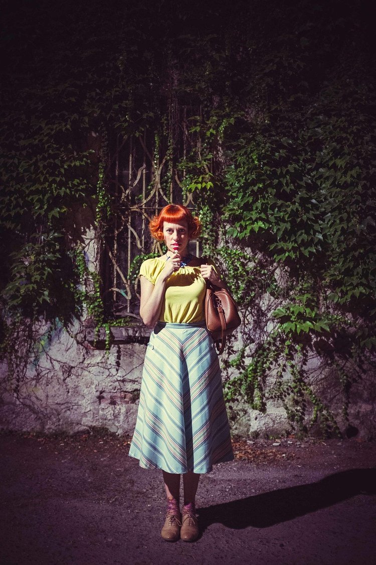 A travel photographer captures an image of a woman with red hair wearing a yellow shirt standing in front of the wall.jpg