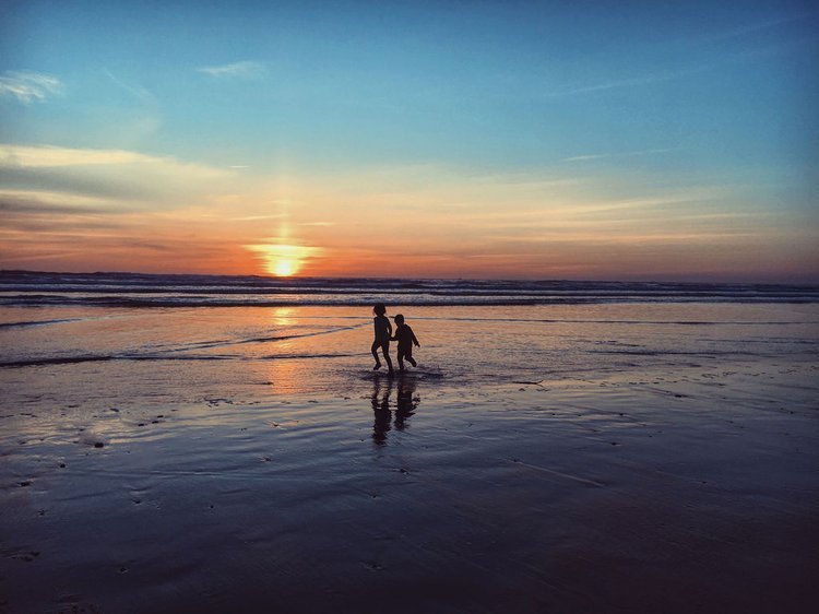 Two children strolling on a sandy beach during sunset, with the sun casting a warm glow on the water showcases the imagination of a travel photographer.jpg