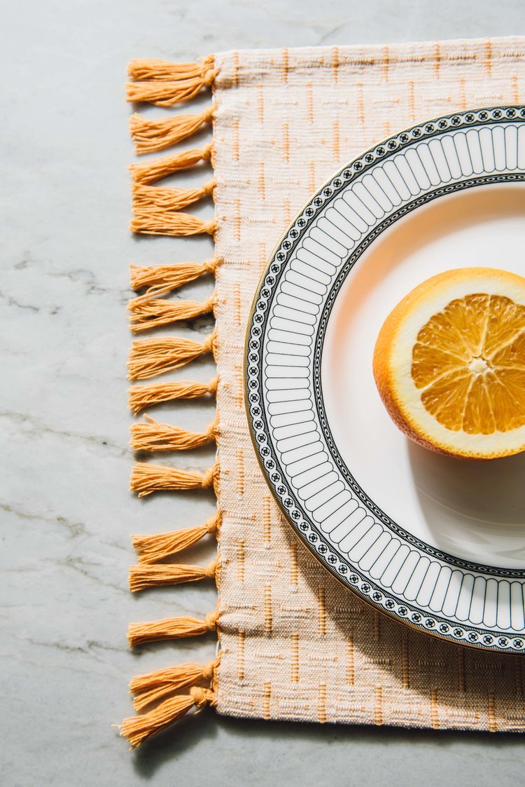 An orange fruit rests on a plate embellished with an elegant tassel, The work of Patrizia a product photographer located in portland.jpg