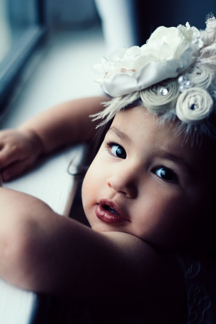 A baby girl wearing a flower headband gazes out of a window in this adorable kid photography.jpg