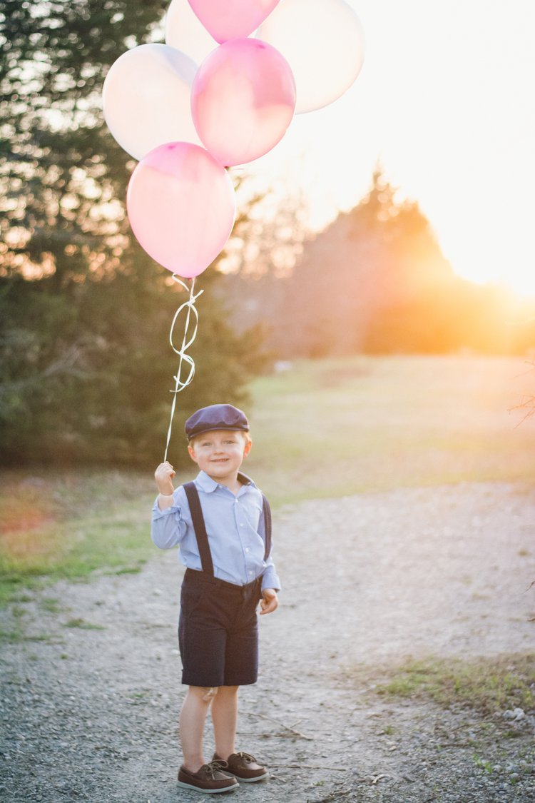 A charming image of a young boy clutching pink balloons at sunset, skillfully captured by a children's portrait photographer.jpg