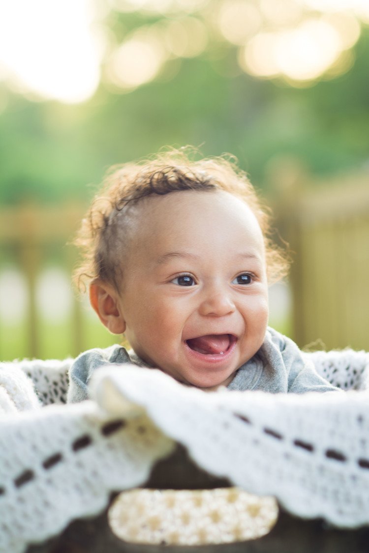 A newborn photographer captures a delightful moment of a baby smiling while sitting in a basket.jpg