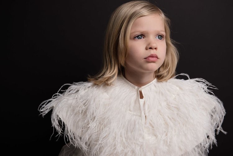 A young girl in a white feather dress, showcasing innocence and elegance.jpg