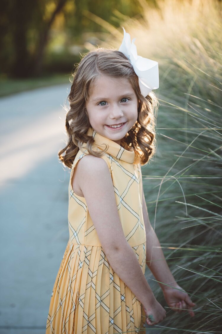 A young girl in a yellow dress stands before tall grass in this children's portrait photograph.jpg