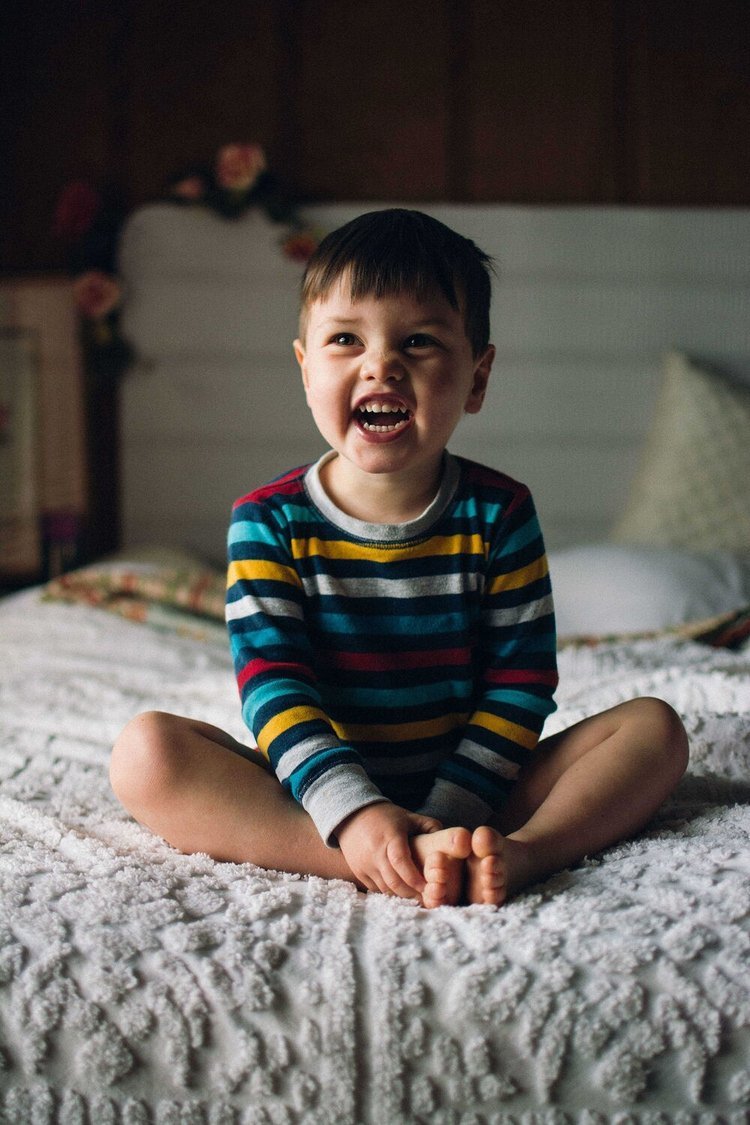 An adorable child with a beaming smile sitting on a bed, captured in a delightful child photography session.jpg