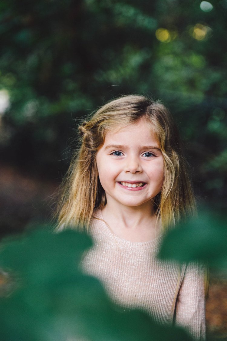 In the woods, a little girl beams with joy as a children's portrait photographer captures her portrait.jpg