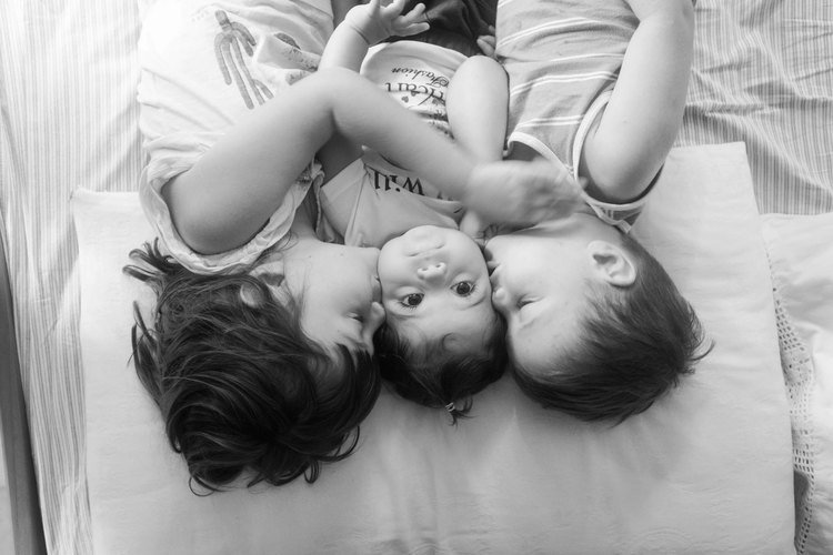 Three children snuggled together in bed, their faces filled with joy and innocence.jpg