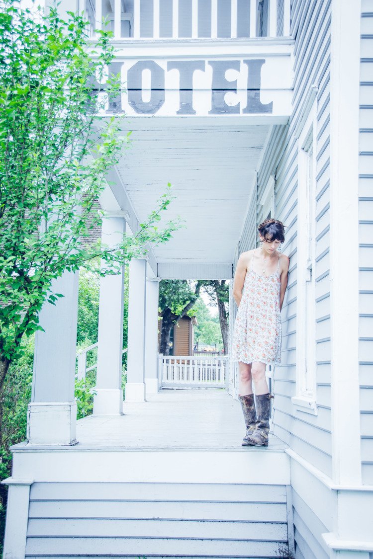 Captured in a lifestyle fashion shot, a woman in a dress and boots strikes a pose on the steps of a hotel.jpg