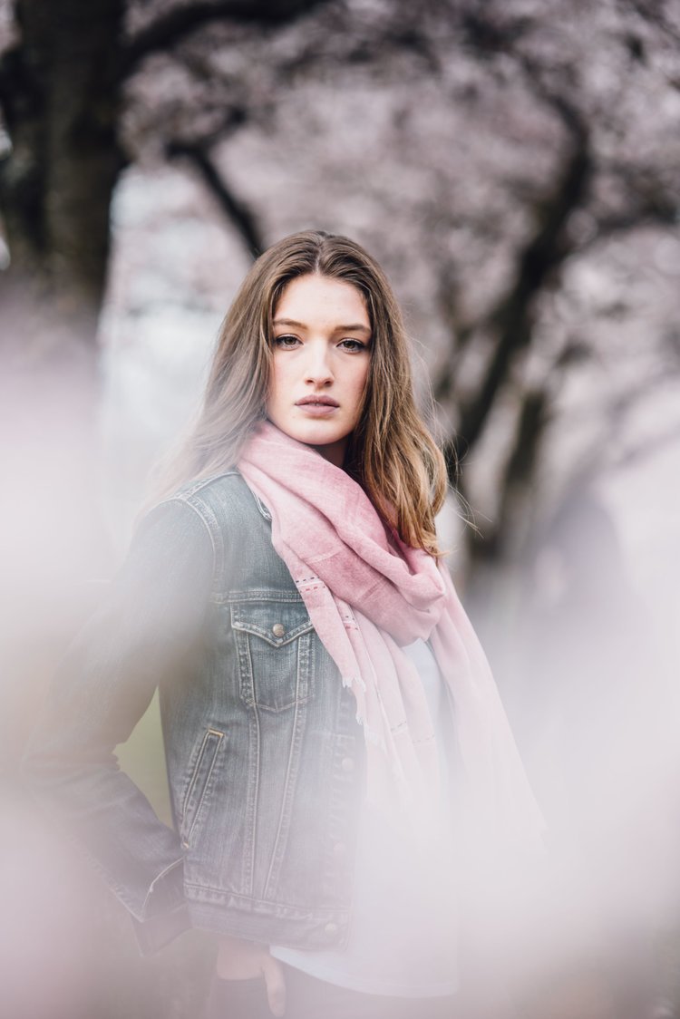 In a commercial lifestyle photograph, a woman wearing a pink scarf poses in front of trees..jpg