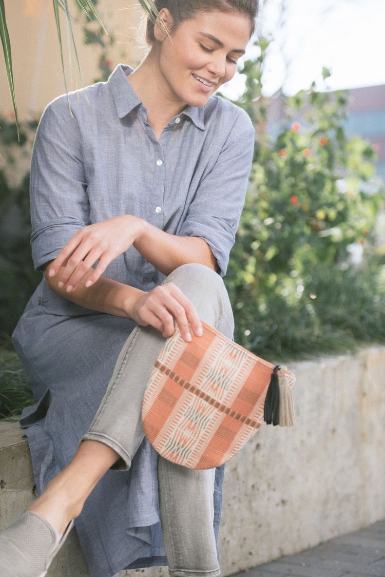 In a lifestyle fashion photograph, a woman sits on a bench, elegantly clutching a purse, exuding style and poise.jpg