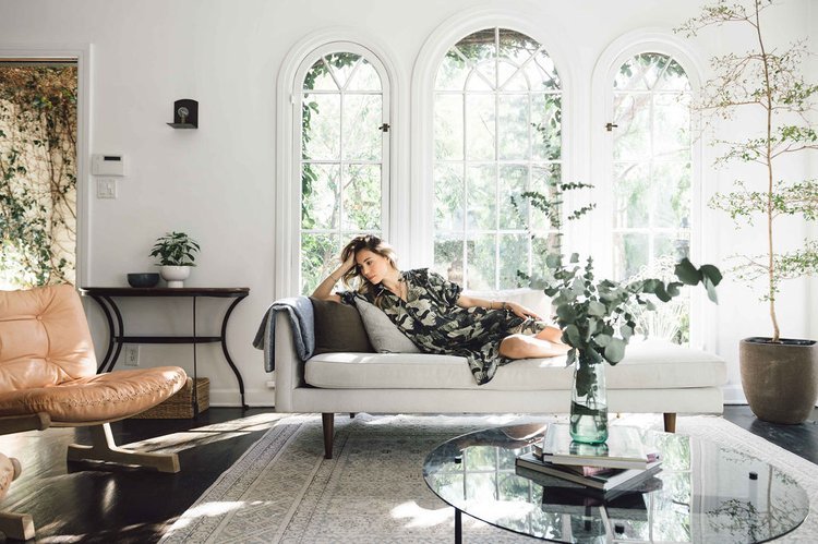 In a living room, a woman elegantly poses on a couch as a lifestyle fashion photographer captures the moment.jpg