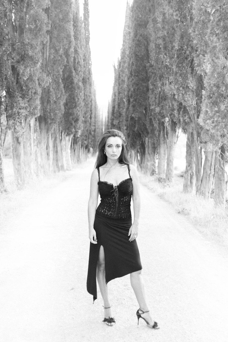 In a photograph by a fashion lifestyle photographer, a woman elegantly poses on a road wearing a black dress.jpg