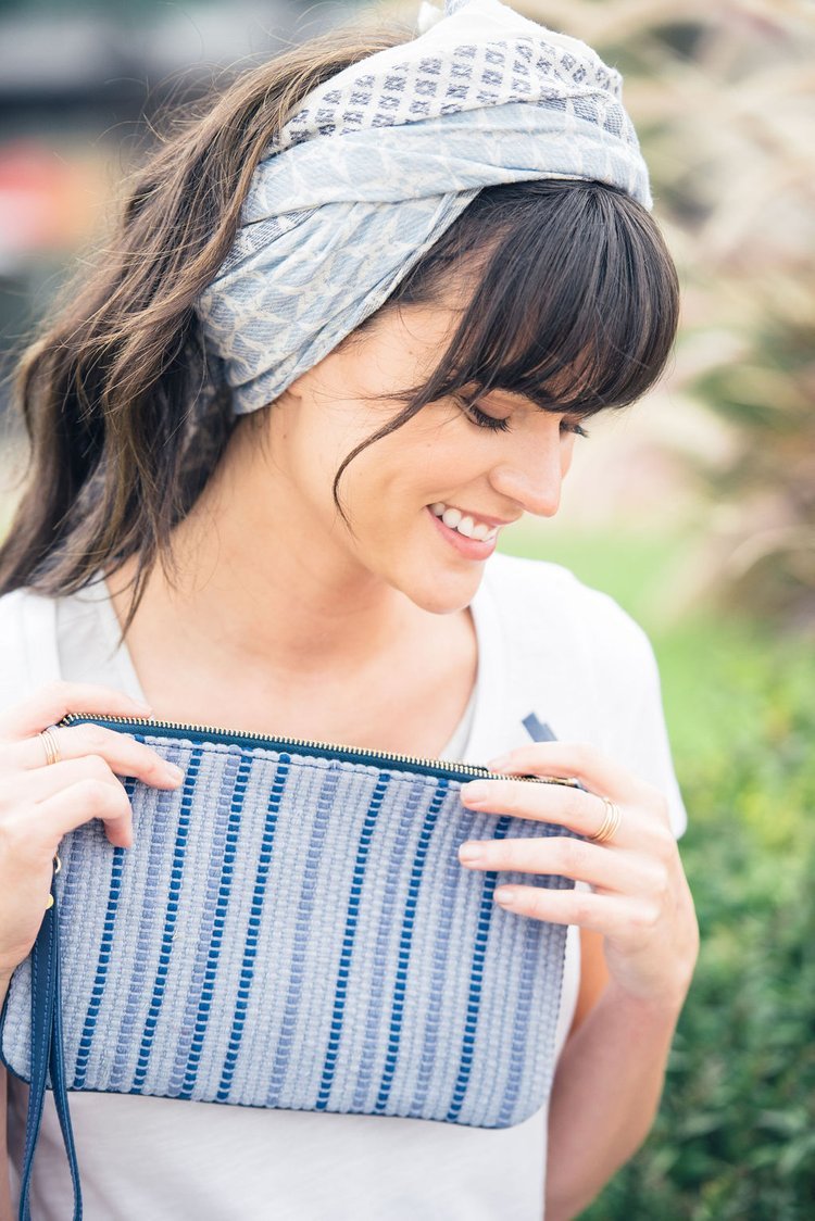 In this lifestyle fashion image, a woman accessorized with a headband gracefully holds a blue and white striped clutch.jpg