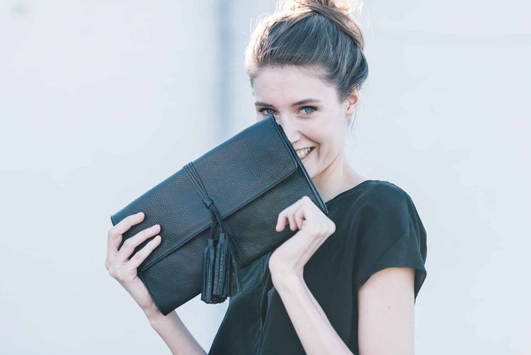 A woman in a black dress elegantly holds a black clutch, exuding sophistication and style.jpg