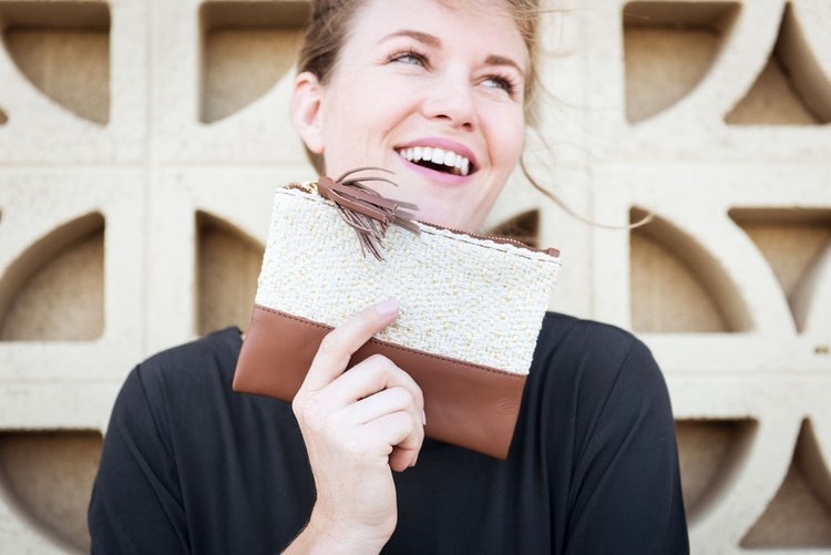 A woman's happy smile is captured by a lifestyle photographer as she holds a chic clutch in white and brown..jpg