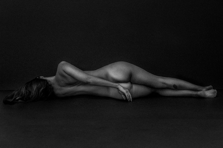 A dark-themed commercial editorial photograph depicting a nude model posing on the floor..jpg